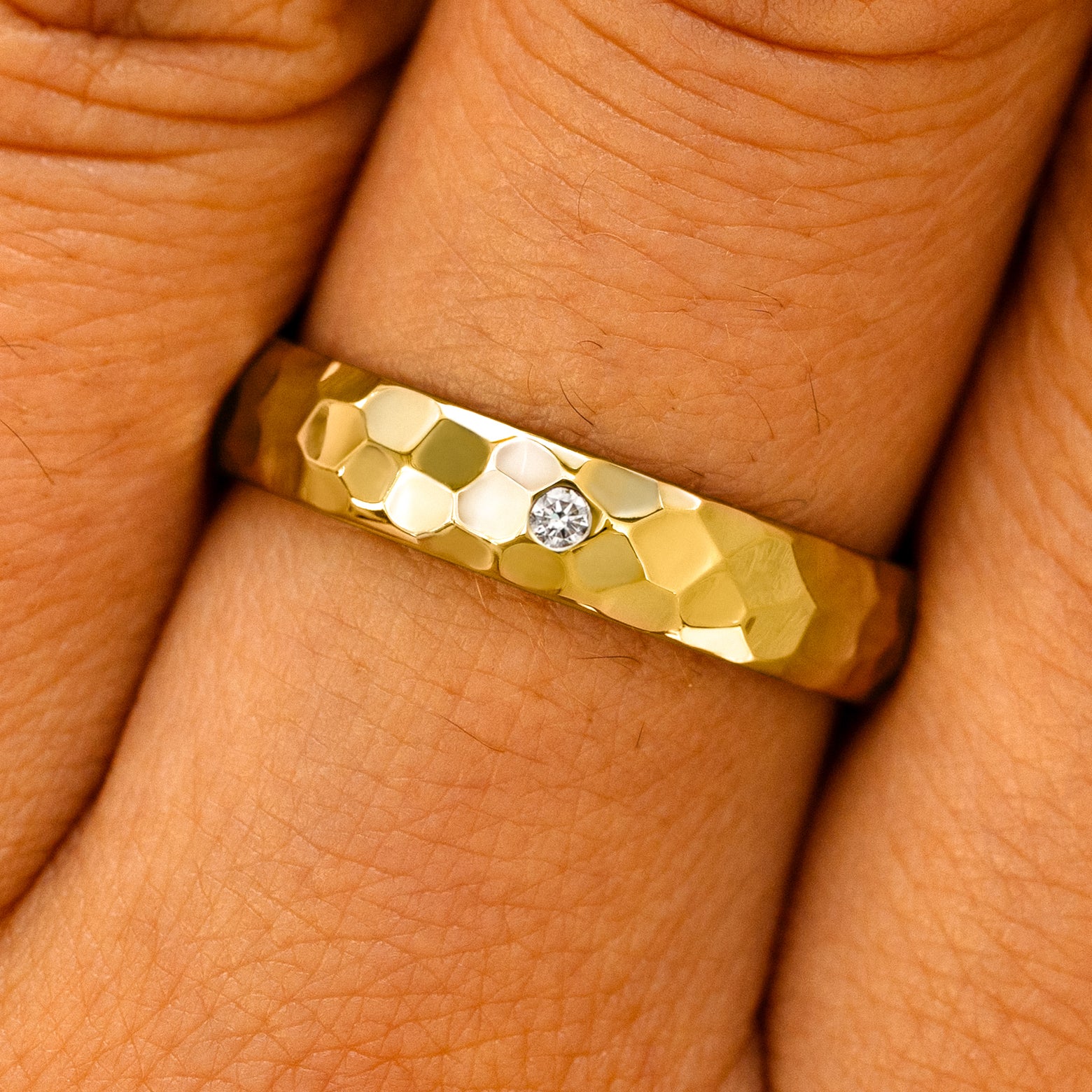 Close up view of a model's fingers wearing a yellow gold 2mm Curvy Hammered Band with center diamonds