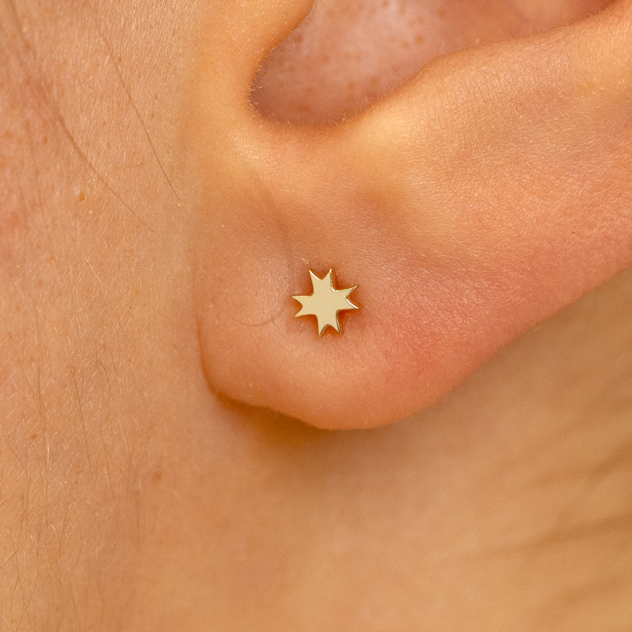 Close up view of a model's ear wearing a champagne gold 8 pointed star earring