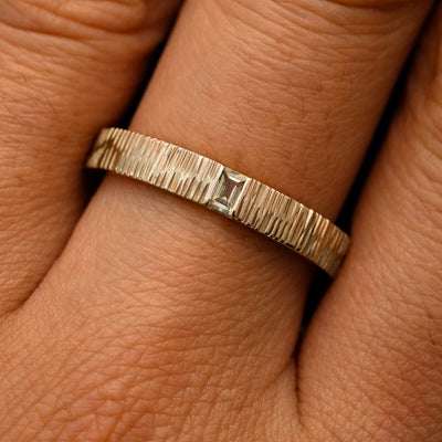 Close up view of a model's fingers wearing a 14k champagne gold Baguette Green Sapphire Wood Band