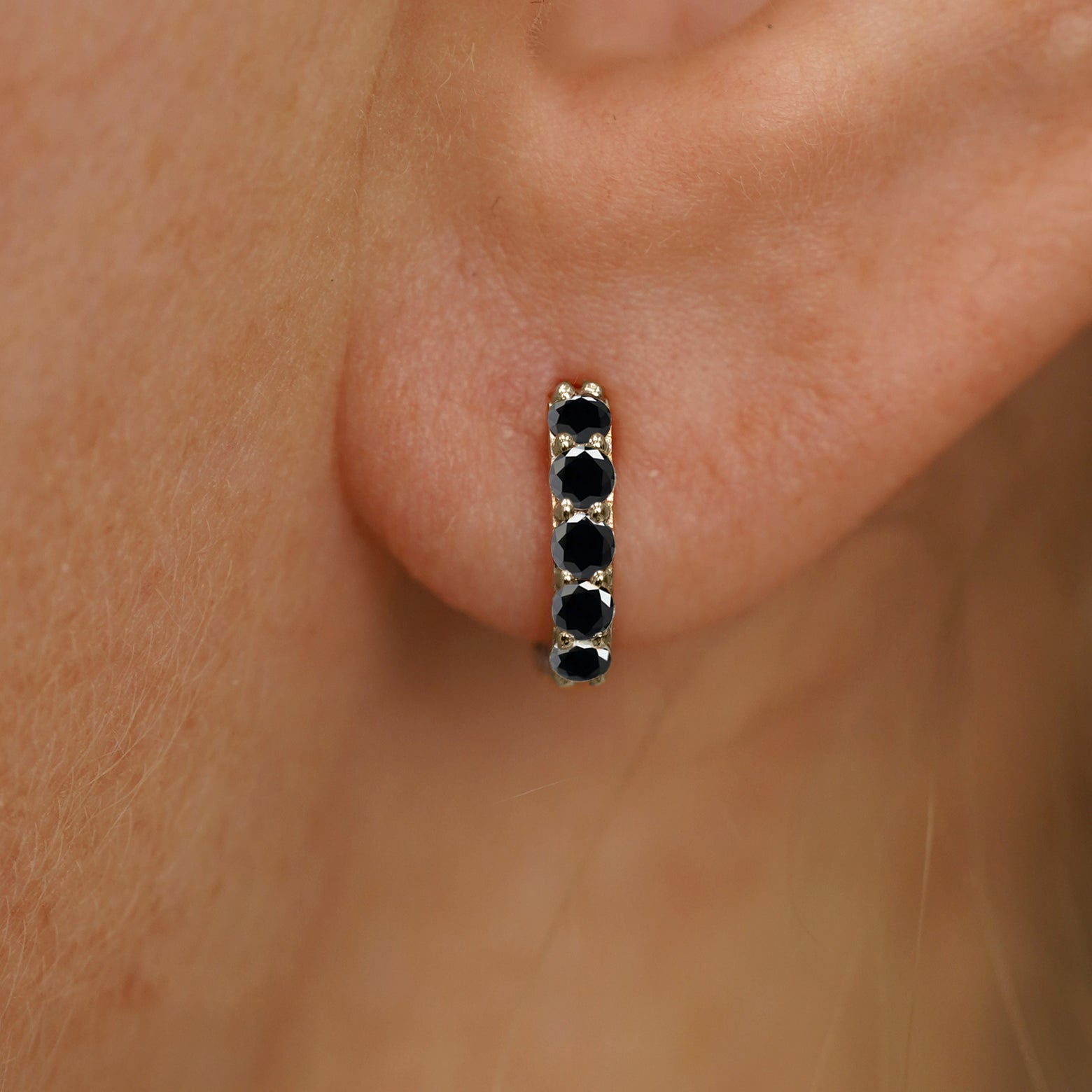 Close up view of a model's ear wearing a champagne gold mini Black Diamond Huggie Hoop