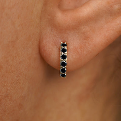 Close up view of a model's ear wearing a champagne gold small Black Diamond Huggie Hoop
