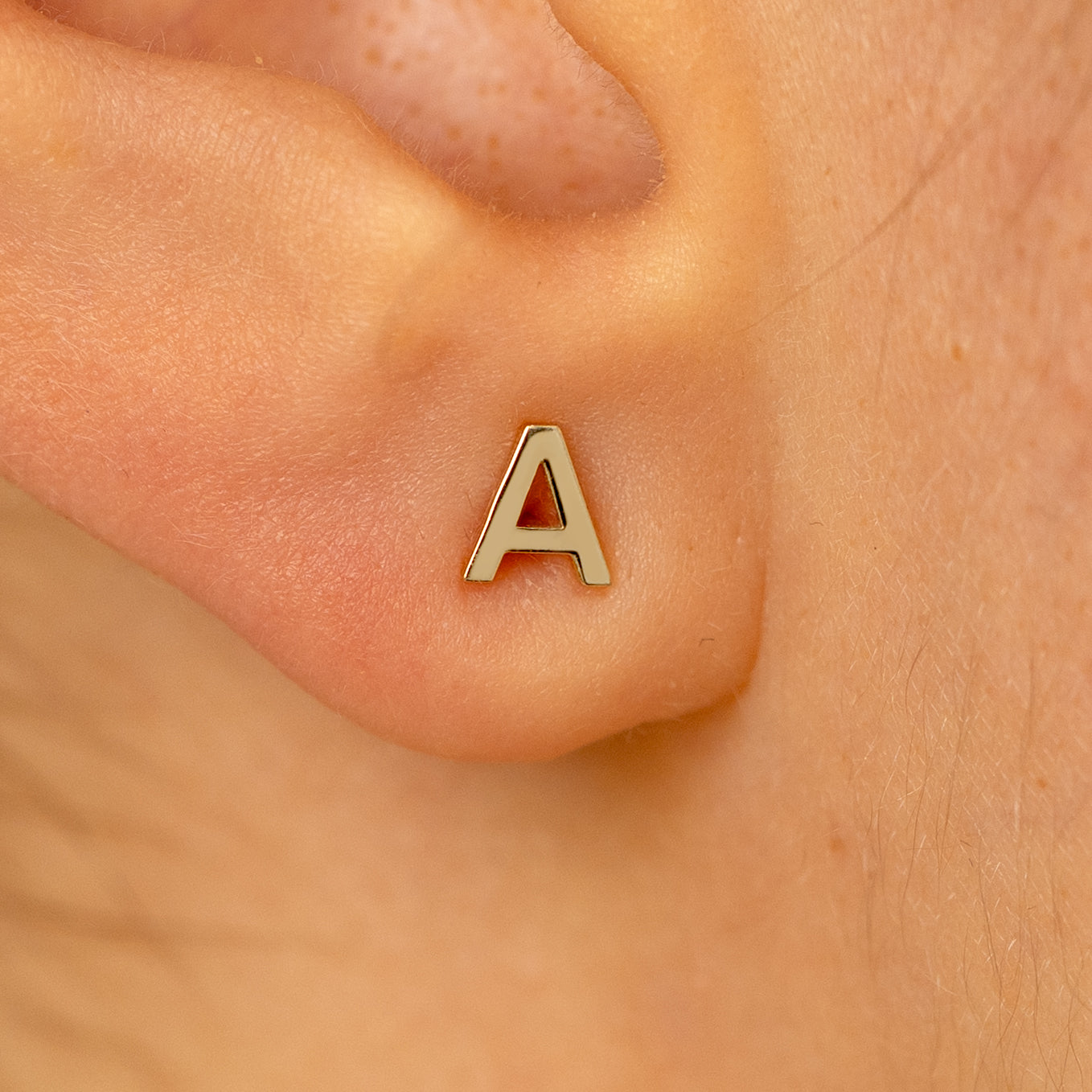 Close up view of a models ear wearing a 14k champagne gold letter A block initial stud earring