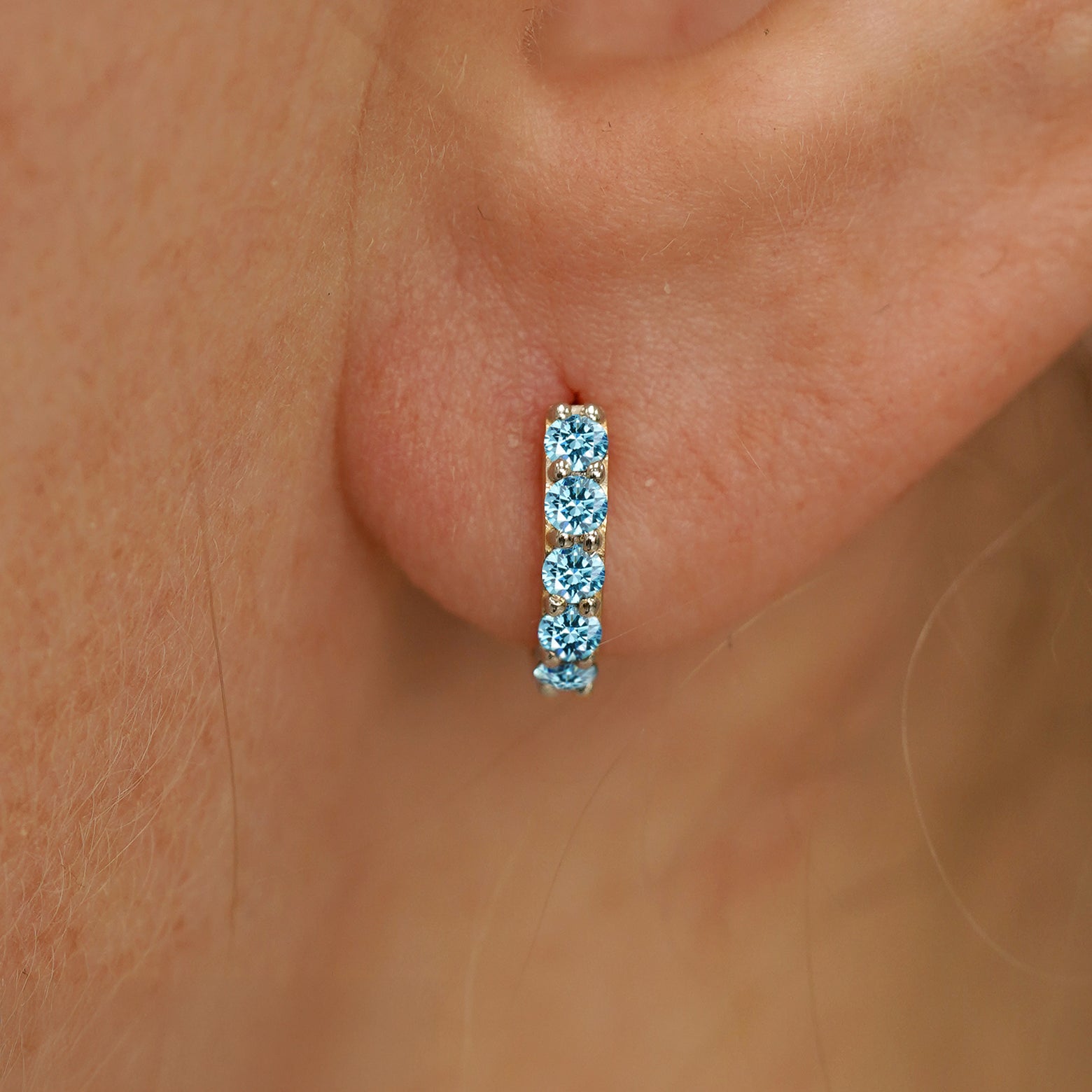 Close up view of a model's ear wearing a champagne gold Mini Light Blue Lab Diamond Huggie Hoop