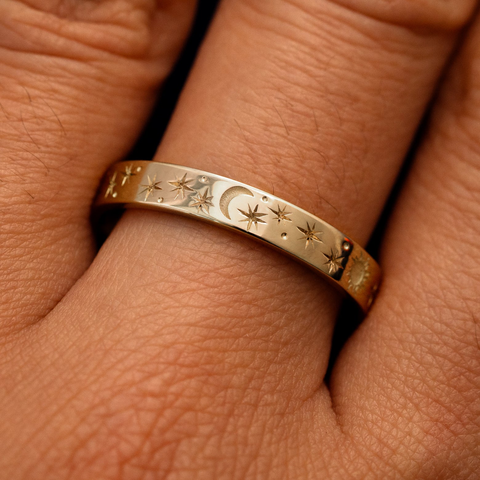 Close up view of a model's fingers wearing a 14k champagne gold Industrial Sun Moon and Stars Band