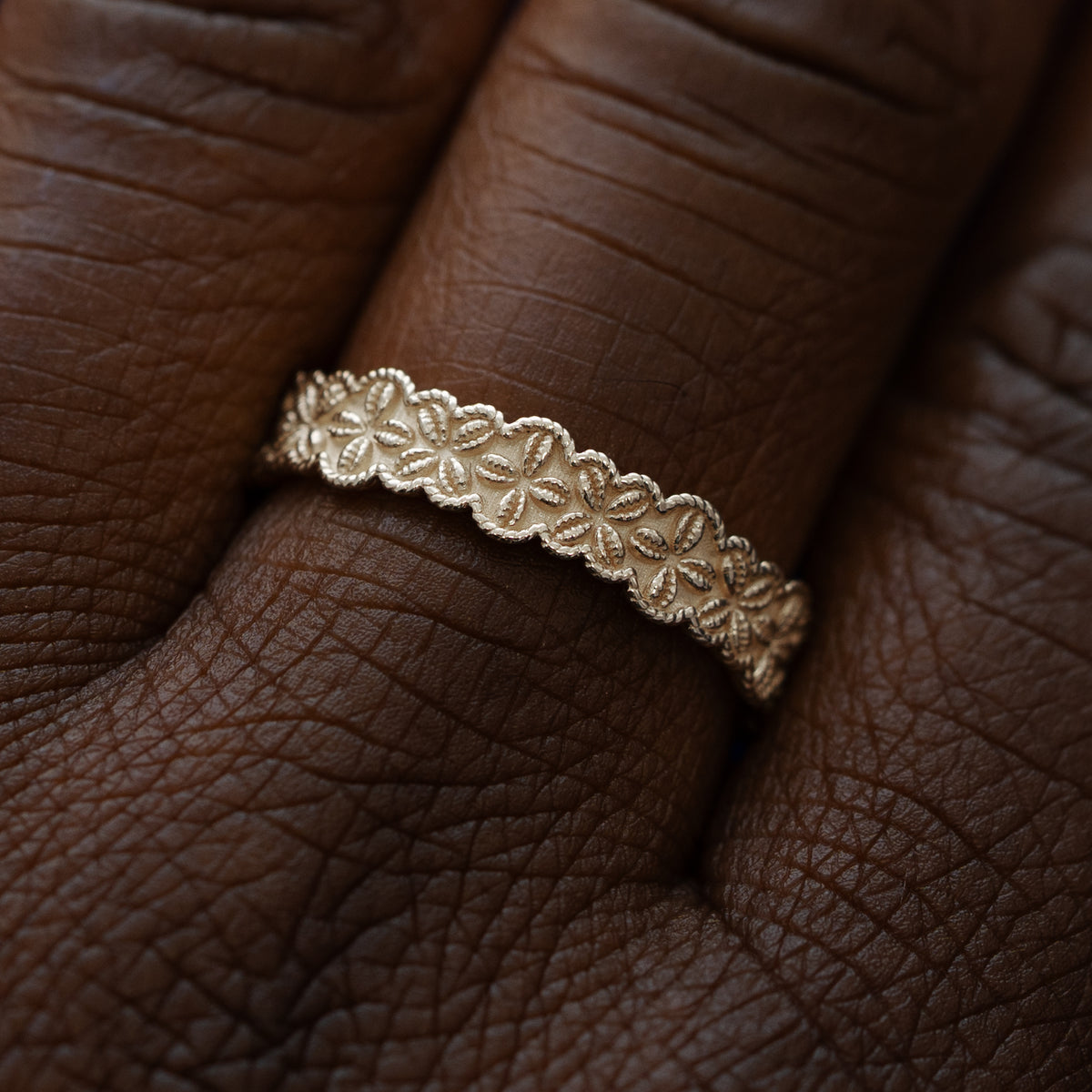 Close up view of a model wearing a solid 14k champagne gold cowrie shell flower and rope band