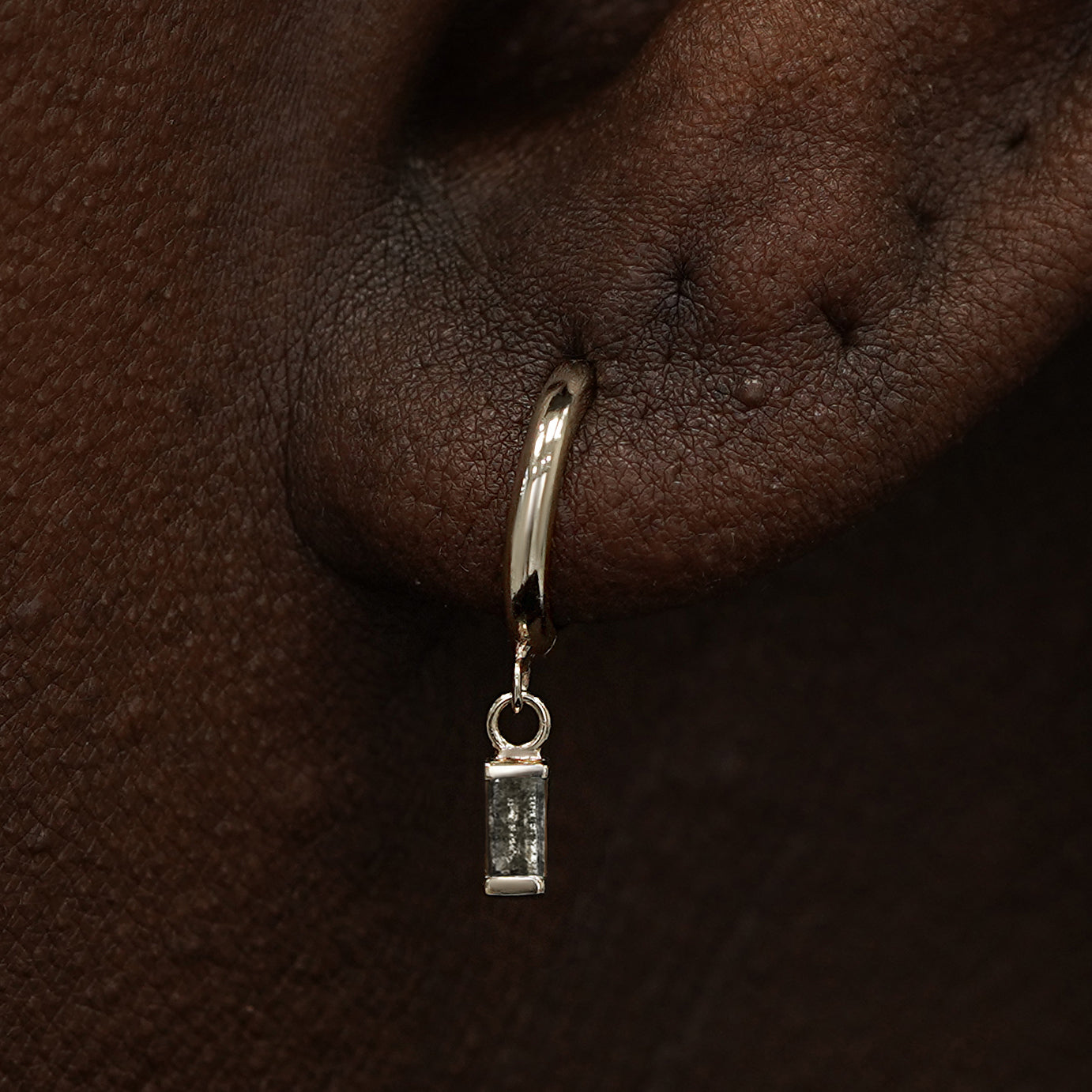 Close up view of a model's ear wearing a champagne gold Baguette Diamond Dangle Huggie Hoop
