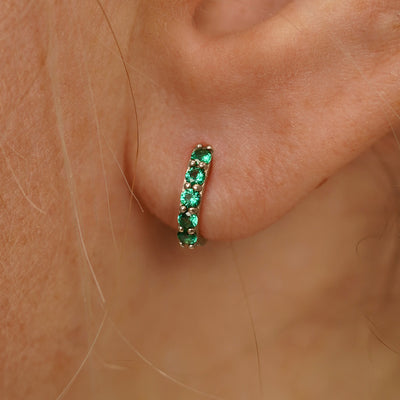 Close up view of a model's ear wearing a champagne gold Mini Emerald Huggie Hoop