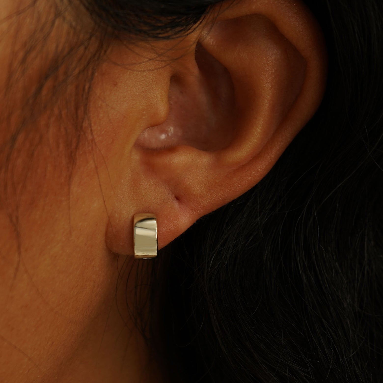 A model's ear wearing a 14 karat champagne gold Extra Wide Huggie Hoop