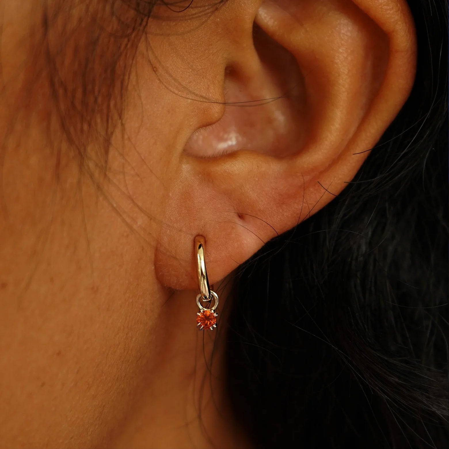 Close up view of a model's ear wearing a champagne gold Fire Opal Charm on a Curvy Huggie Hoop