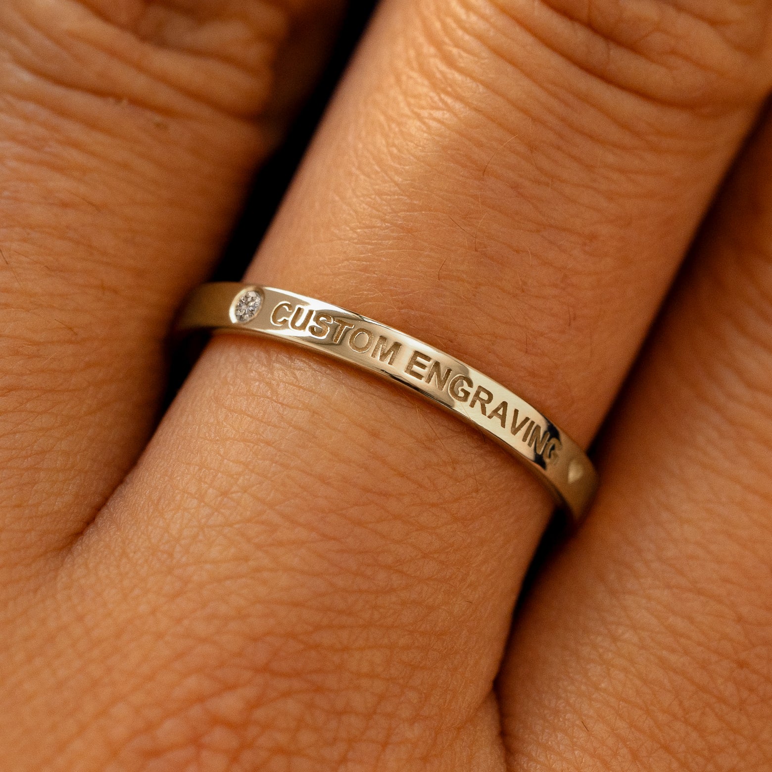 A model's finger wearing a diamond champagne gold flush gemstone industrial band the words custom engraving on the top