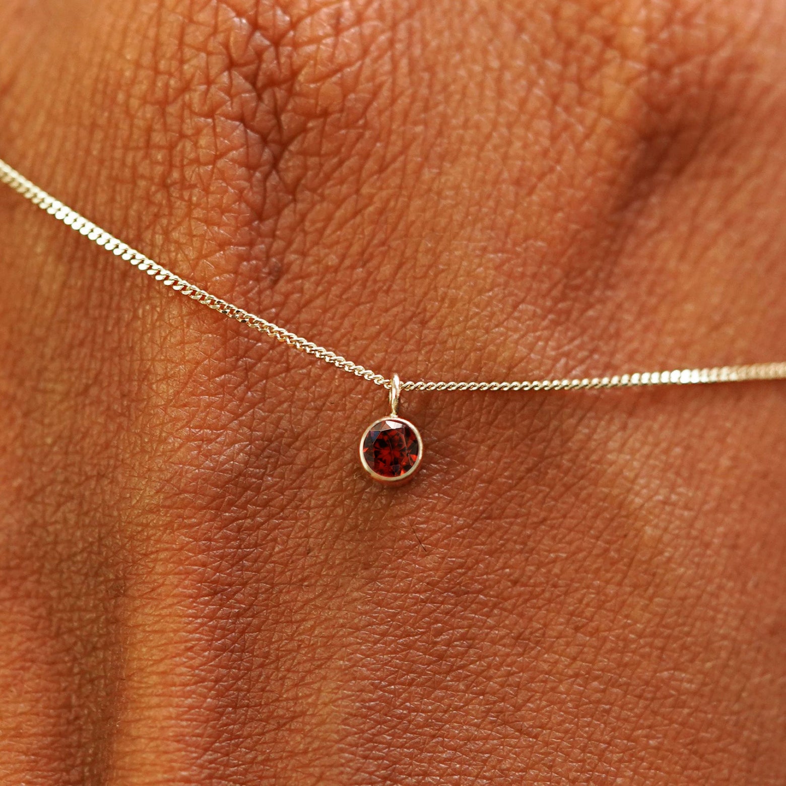 Close up view of a 14k champagne gold Garnet Necklace draped across the back of a model's hand