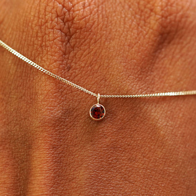 Close up view of a 14k champagne gold Garnet Necklace draped across the back of a model's hand