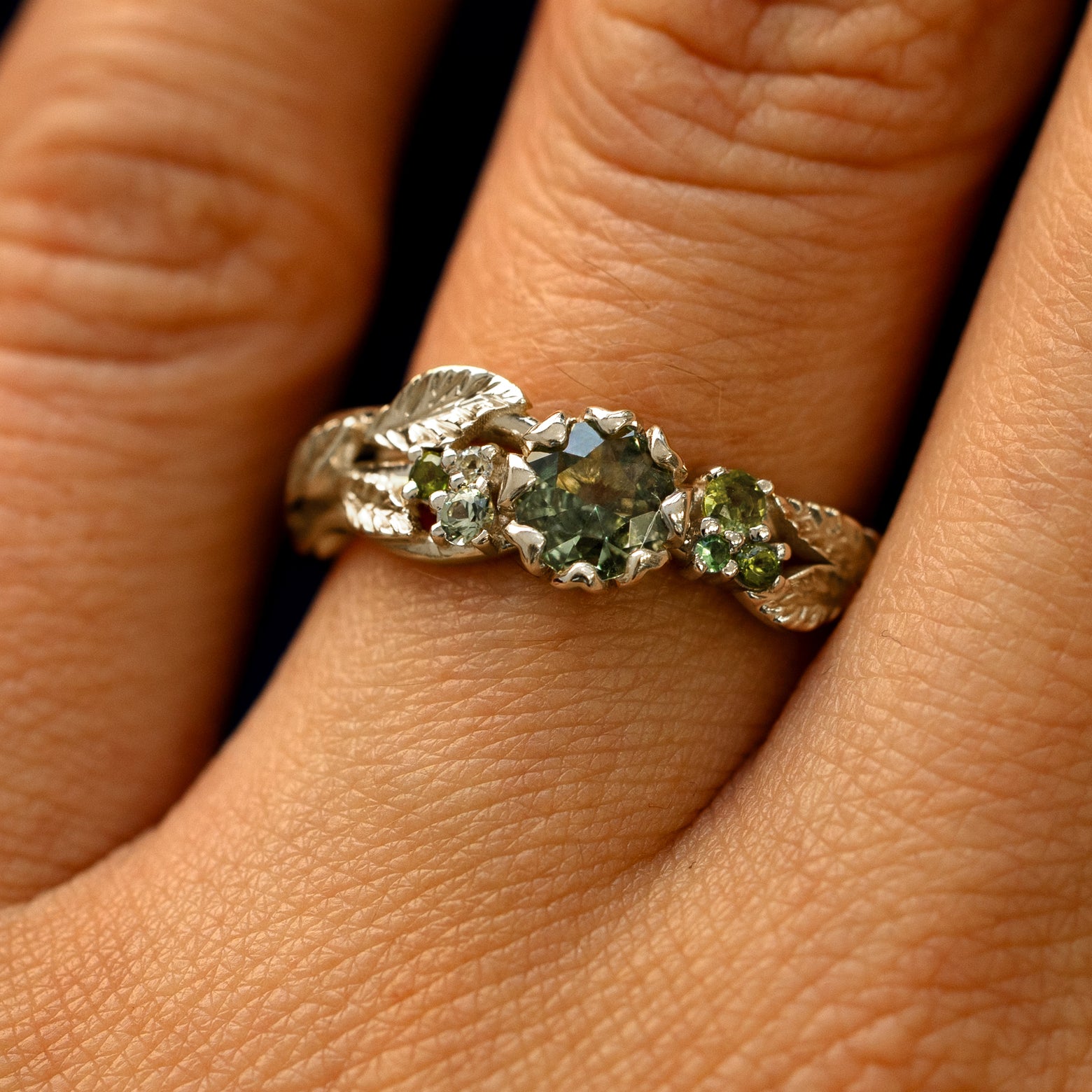 Close up view of a model's fingers wearing a 14k champagne gold Green Sapphire Leaves and Vines Ring