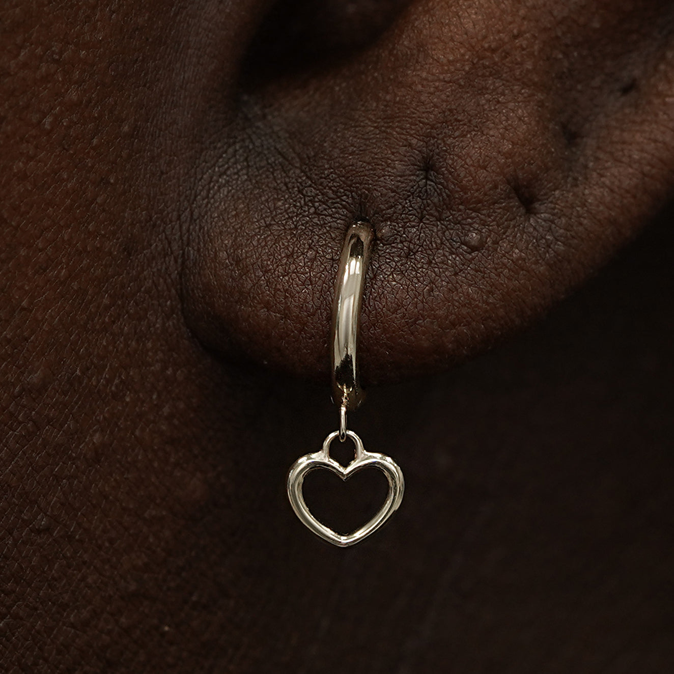 Close up view of a model's ear wearing a champagne gold Heart Charm Huggie Hoop