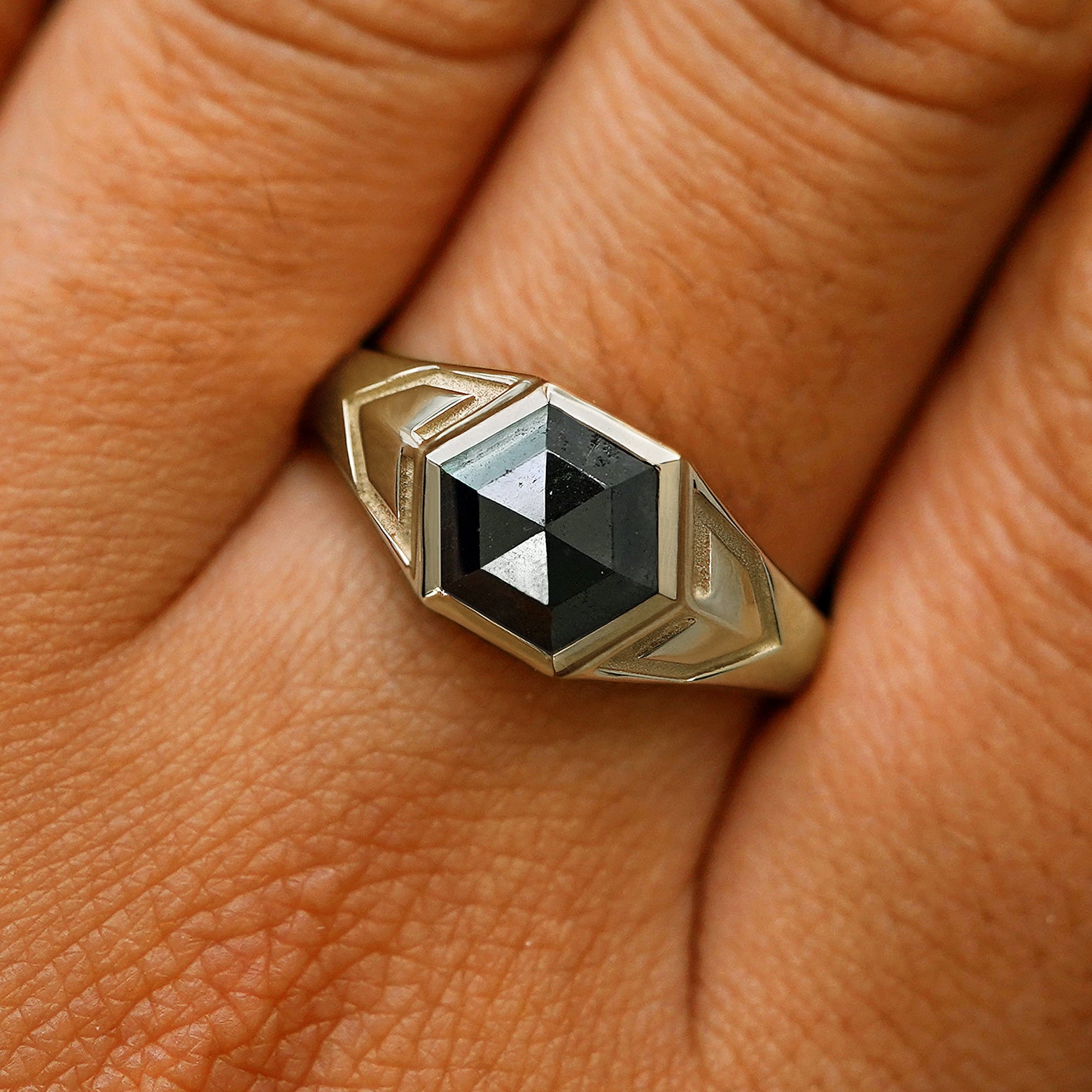 Close up view of a model's fingers wearing a 14k champagne gold hexagon black diamond engraved transformation ring
