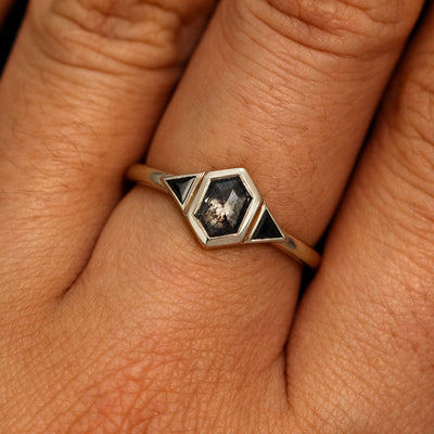 A model's hand wearing a 14k champagne gold Hexagon Salt and Pepper and Triangle Black Diamond Three Stone Ring