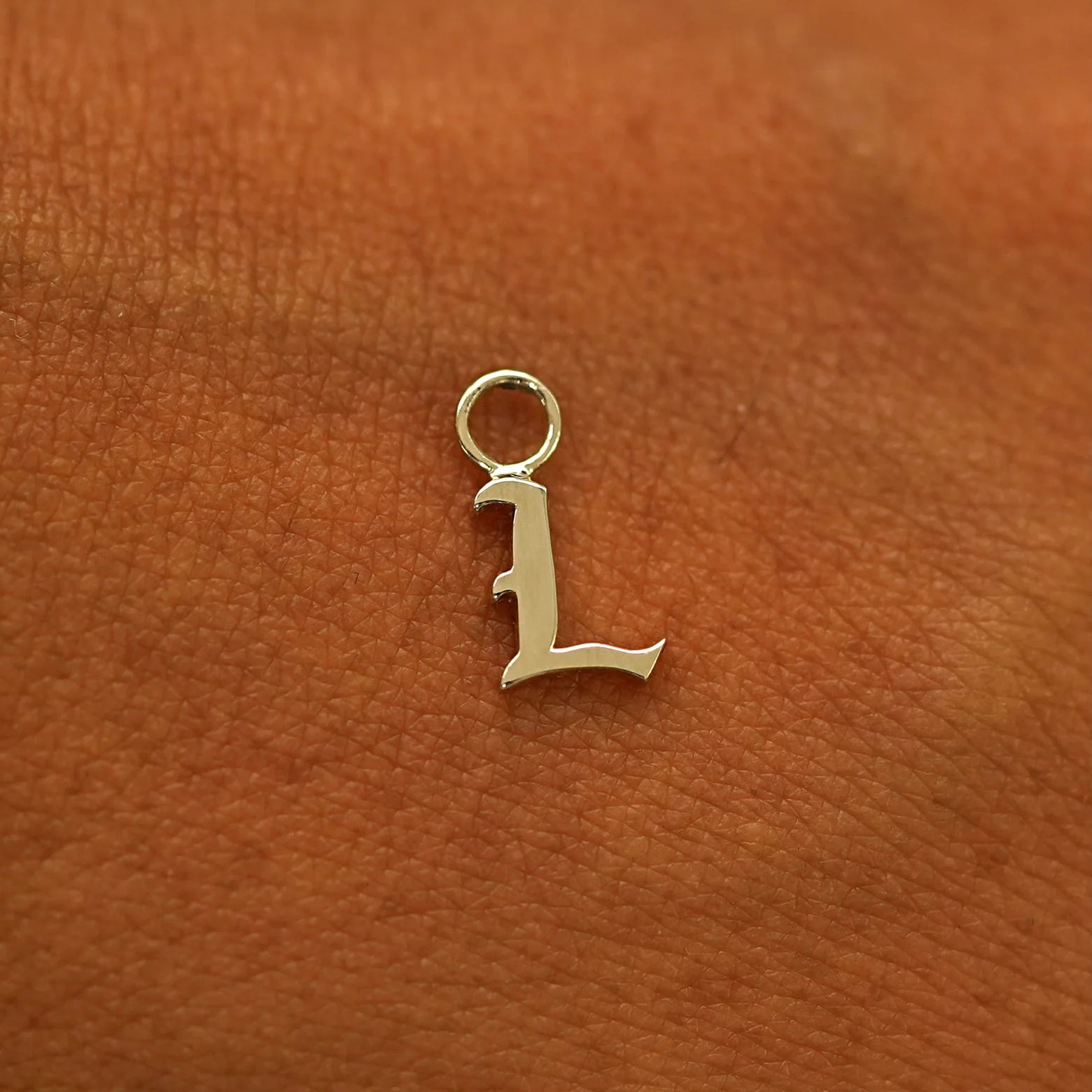 A solid 14k gold Initial Charm for earring in the letter L laying on the back of a model's hand