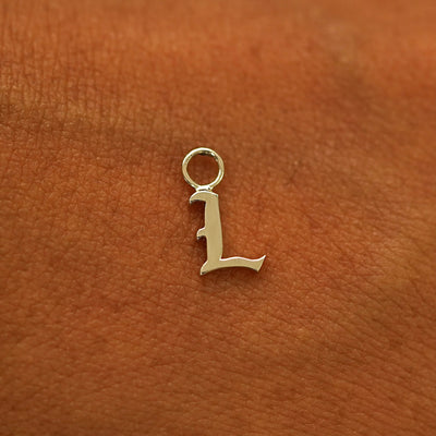 A solid 14k gold Initial Charm for earring in the letter L laying on the back of a model's hand
