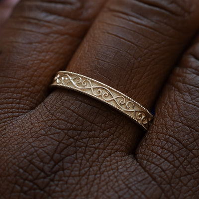 Close up view of a model wearing a solid 14k champagne gold milgrain scroll band