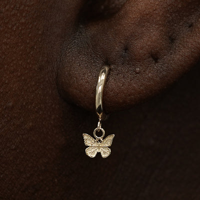 Close up view of a model's ear wearing a champagne gold Mini Butterfly Dangle Huggie Hoop