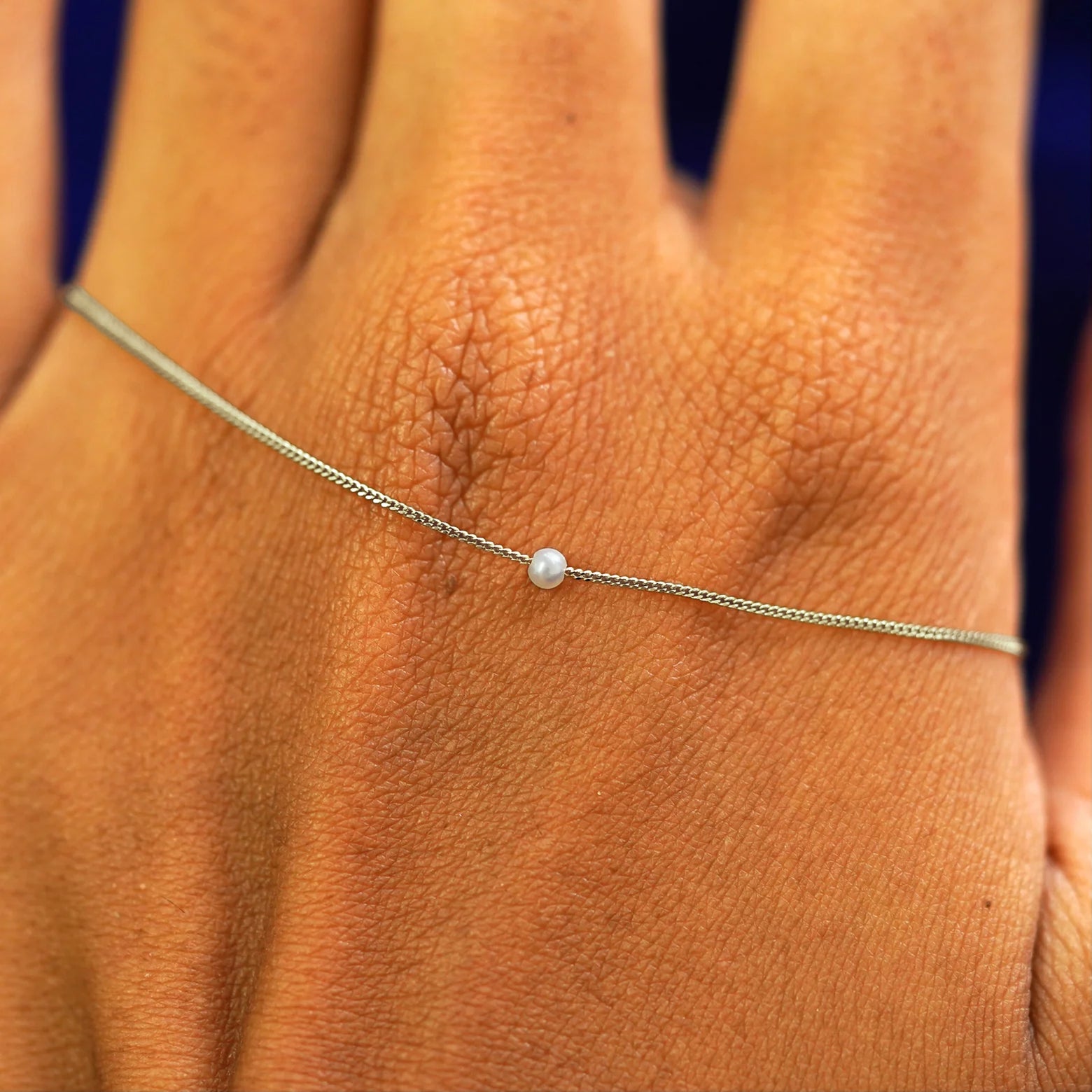 A champagne gold 2mm pearl slide bracelet resting on the back of a model's hand
