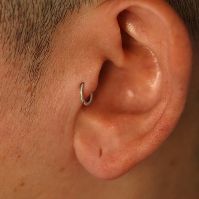 A model's ear wearing a 14k champagne gold Mini Seamless Huggie Hoop in a tragus piercing