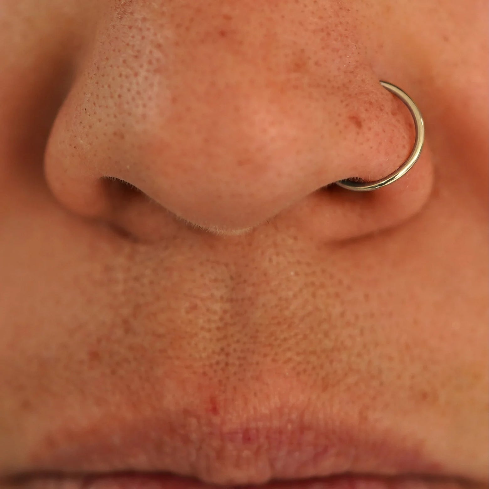 Close up view of a model's nose wearing a 14k champagne gold Nose Ring Hoop