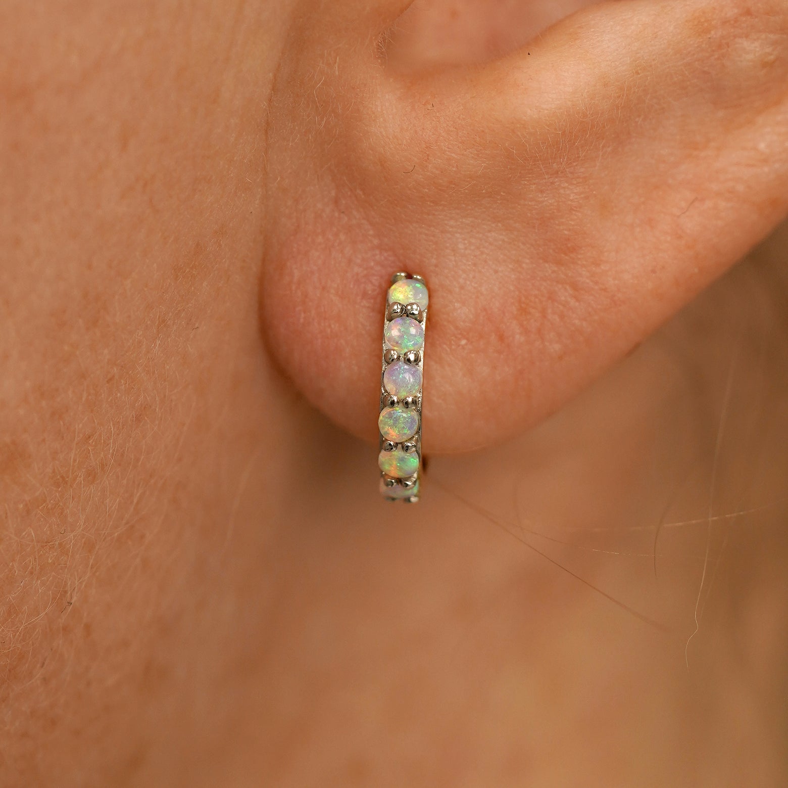 Close up view of a model's ear wearing a champagne gold Small Opal Huggie Hoop