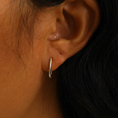 A model's ear wearing a 14 karat champagne gold Oval Huggie Hoop