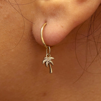 Close up view of a model's ear wearing a champagne gold Palm Tree Charm on a Small Seamless Huggie Hoop