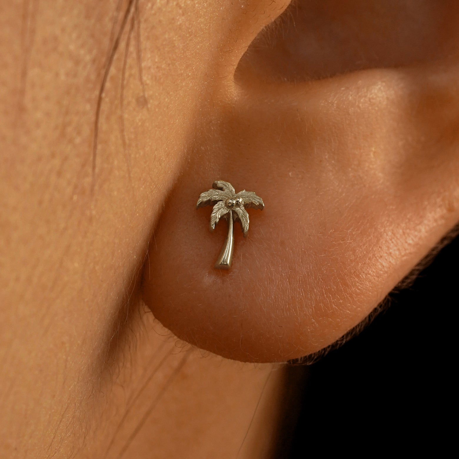 Close up view of a model's ear wearing a 14k champagne gold Palm Tree Earring