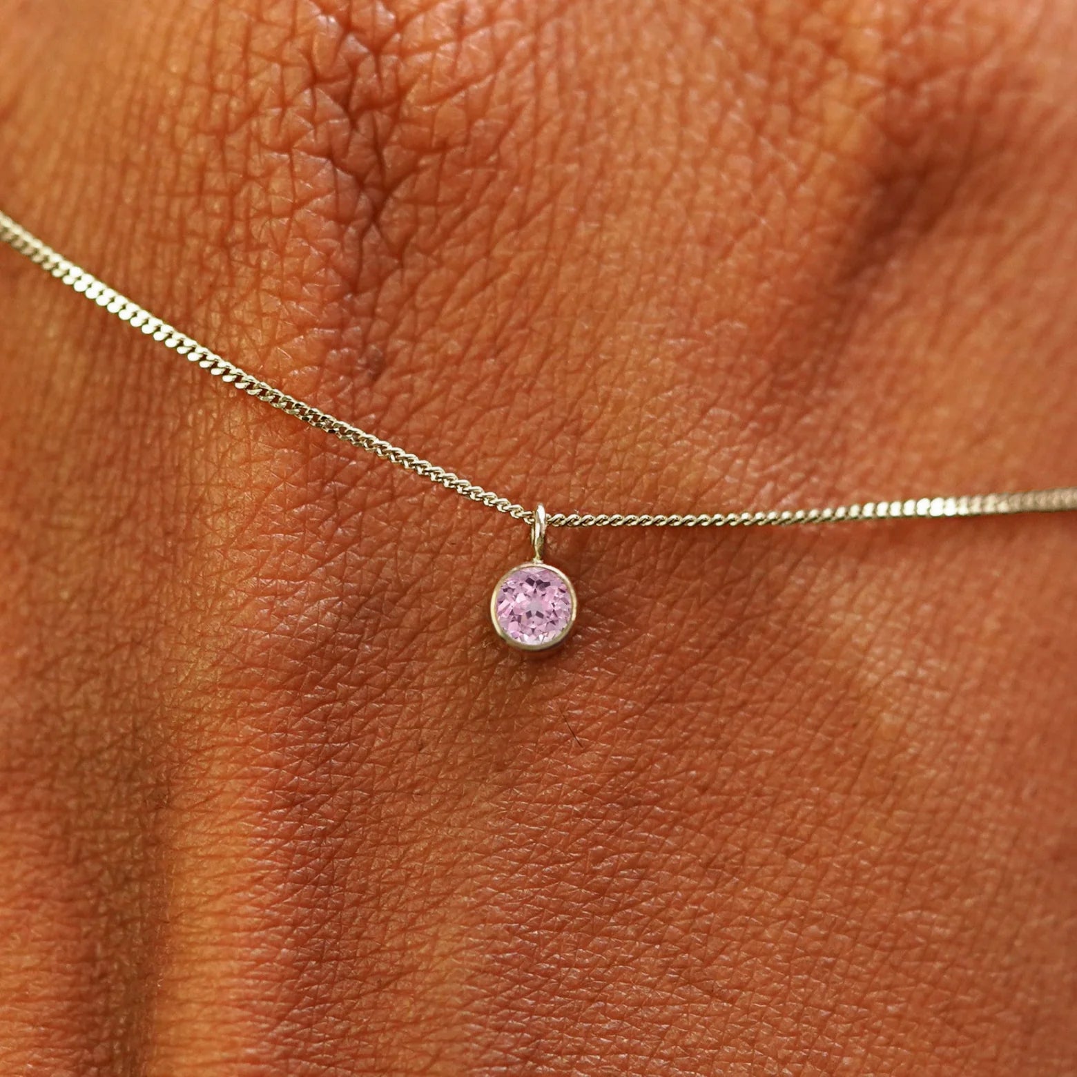Close up view of a 14k champagne gold Pink Sapphire Necklace draped across the back of a model's hand