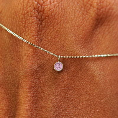 Close up view of a 14k champagne gold Pink Sapphire Necklace draped across the back of a model's hand
