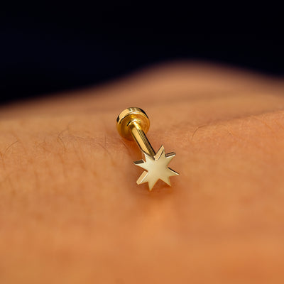 A champagne gold 8 pointed star flatback piercing with yellow gold backing on a models hand