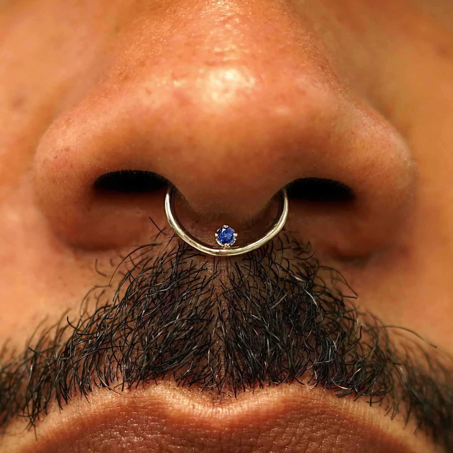 Close up view of a model's nose wearing a 14k champagne gold sapphire Raised Gemstone Septum