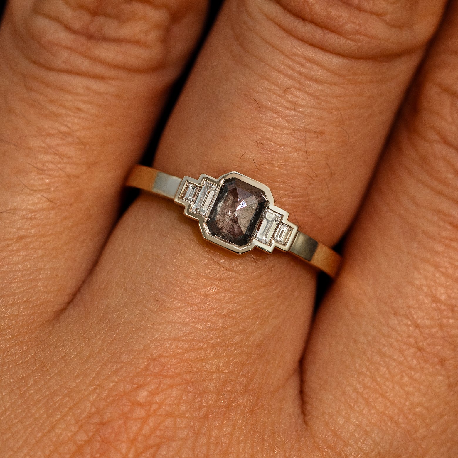 Close up view of a model's hand wearing a 14k champagne gold Emerald Cut Salt and Pepper and Clear Baguette Diamond Ring