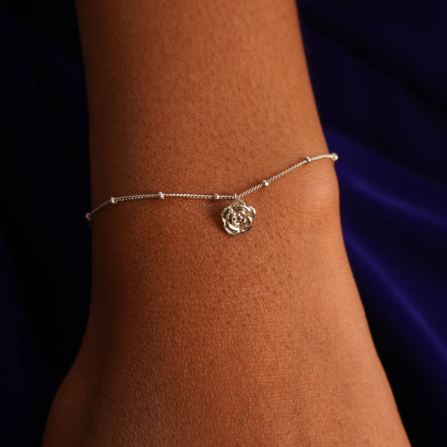 Close up view of a model's wrist wearing a champagne gold Rose Charm on a Beaded Essential Chain