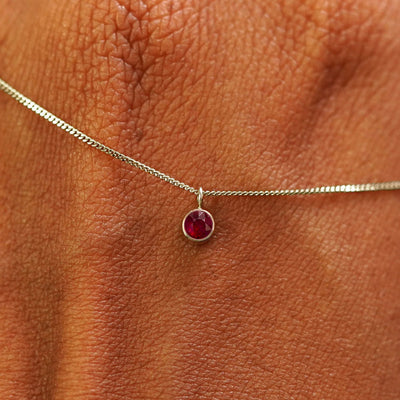 Close up view of a 14k champagne gold Ruby Necklace draped across the back of a model's hand