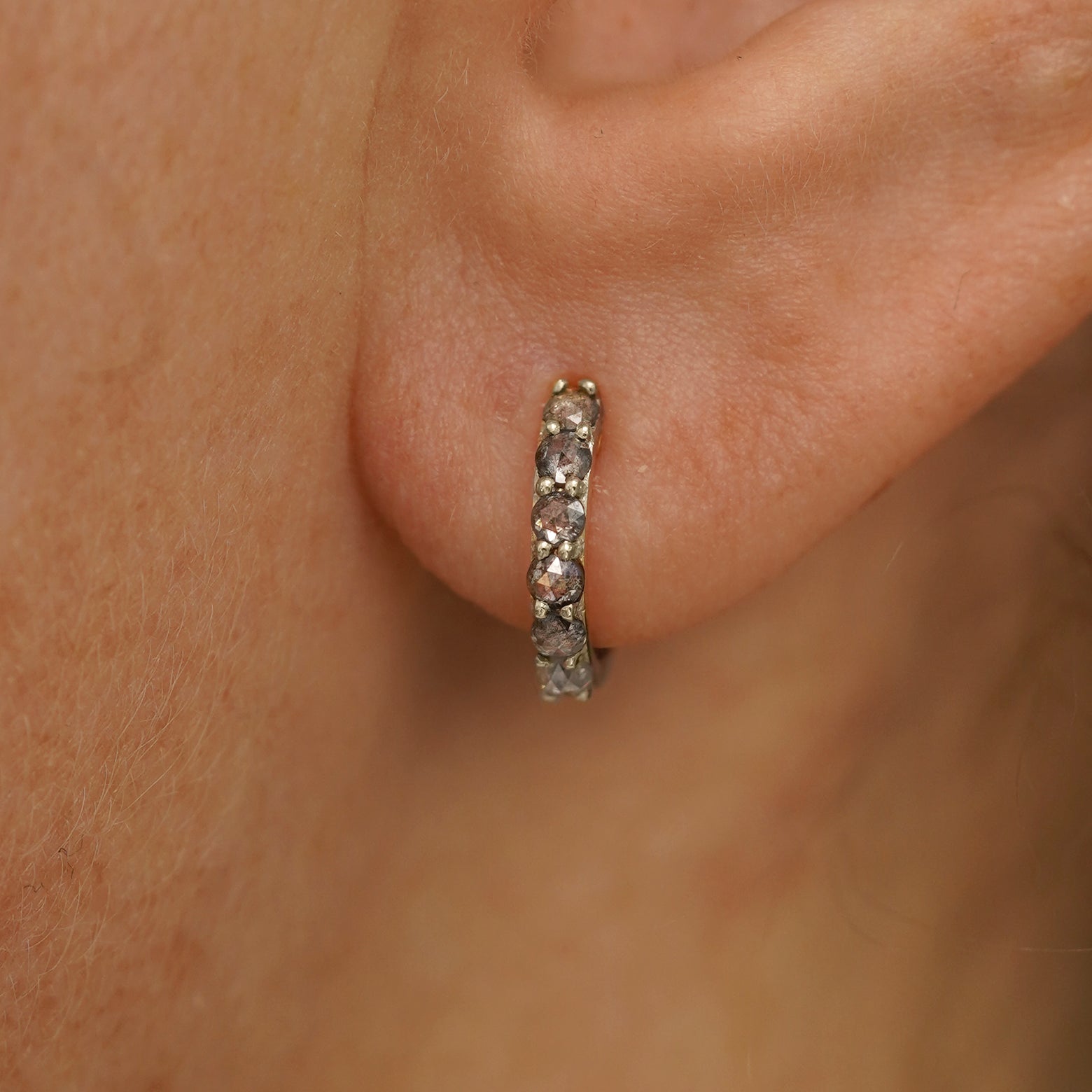 Close up view of a model's ear wearing a champagne gold Small Salt and Pepper Diamond Huggie Hoop