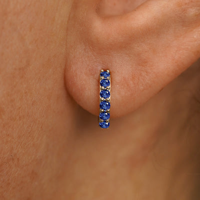 Close up view of a model's ear wearing a champagne gold Small Blue Sapphire Huggie Hoop