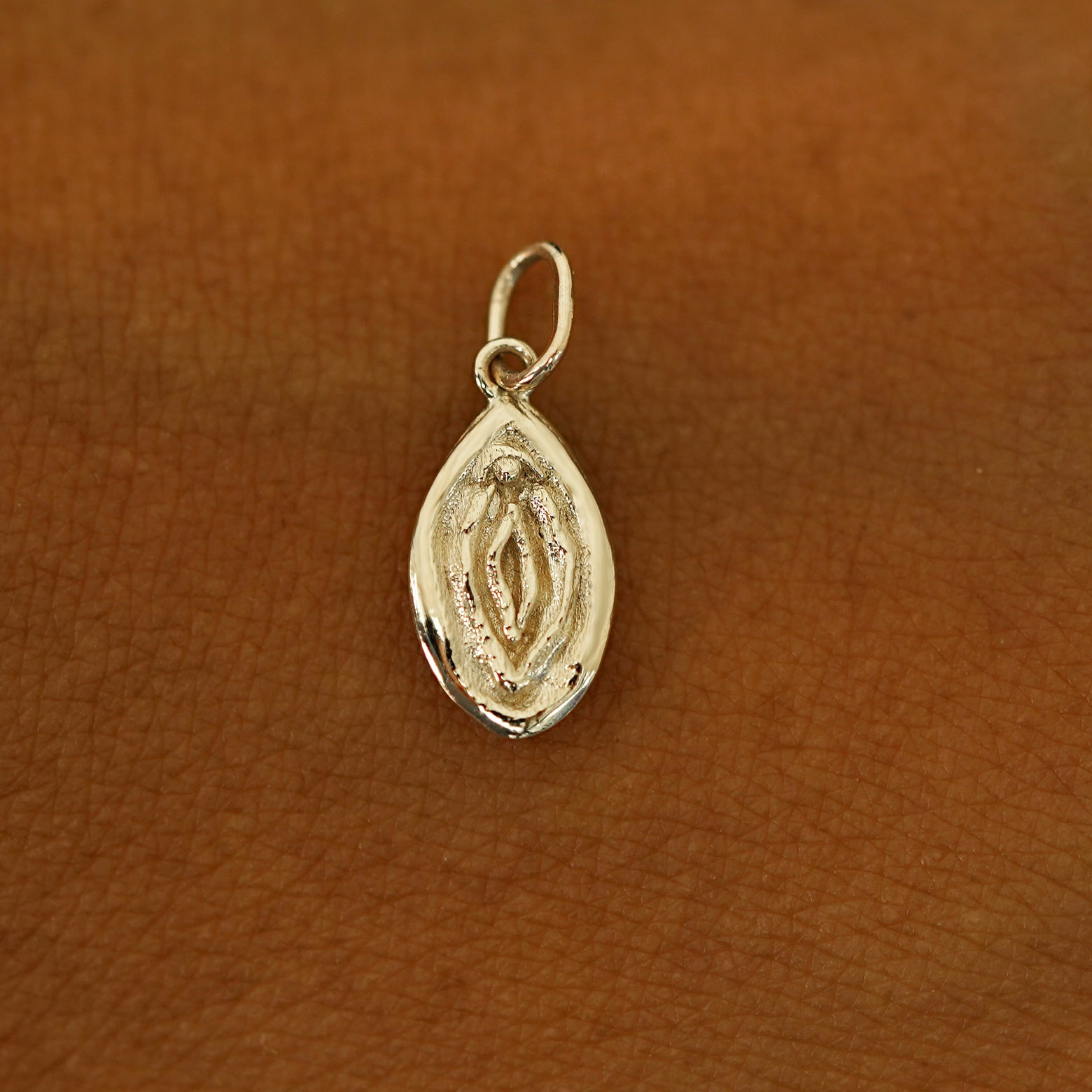 A solid 14k champagne gold Vulva Charm resting on the back of a model's hand