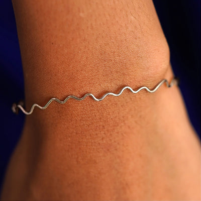 Close up view of a model's wrist wearing a 14k champagne gold Wave Bangle Bracelet