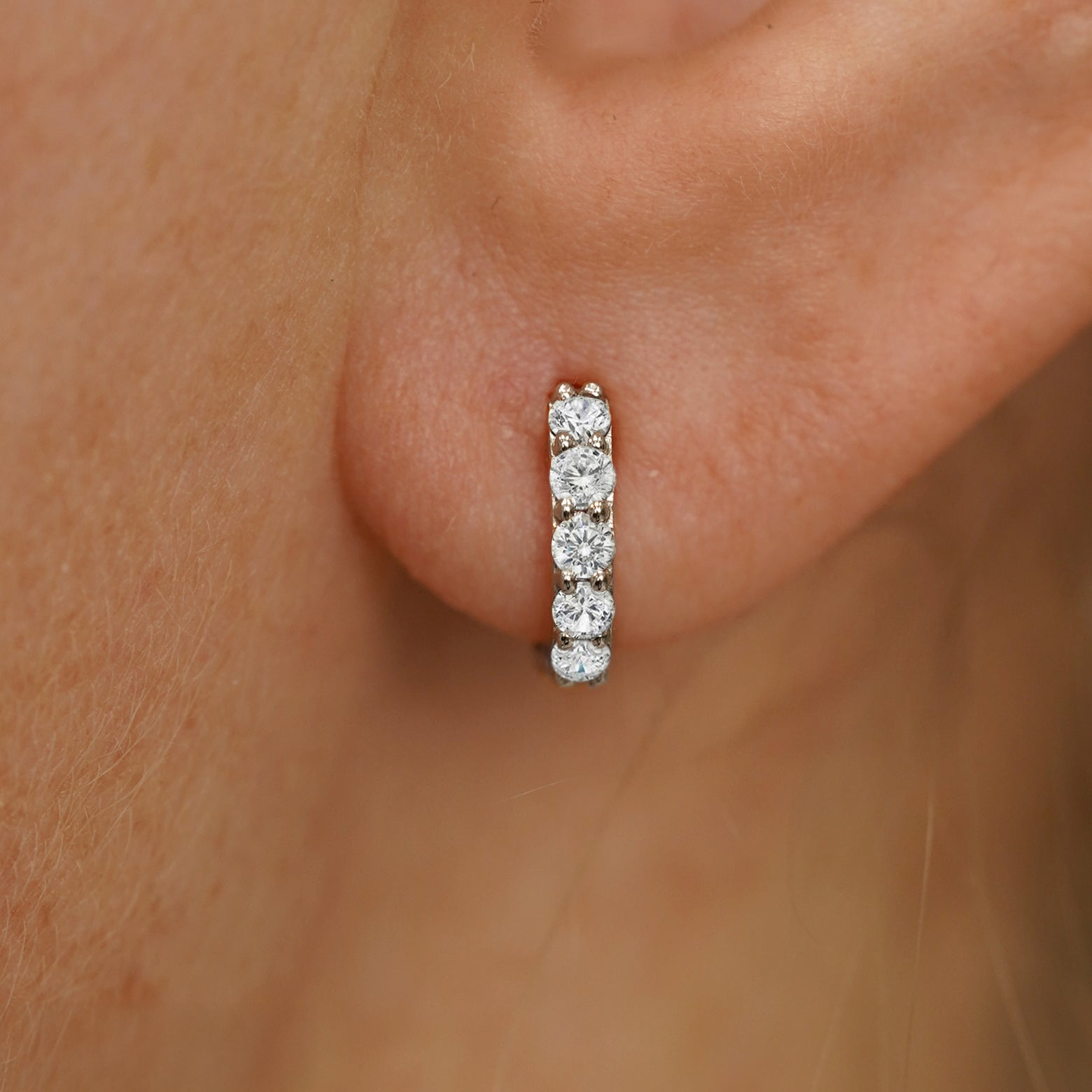 Close up view of a model's ear wearing a champagne gold Mini Lab White Diamond Huggie Hoop