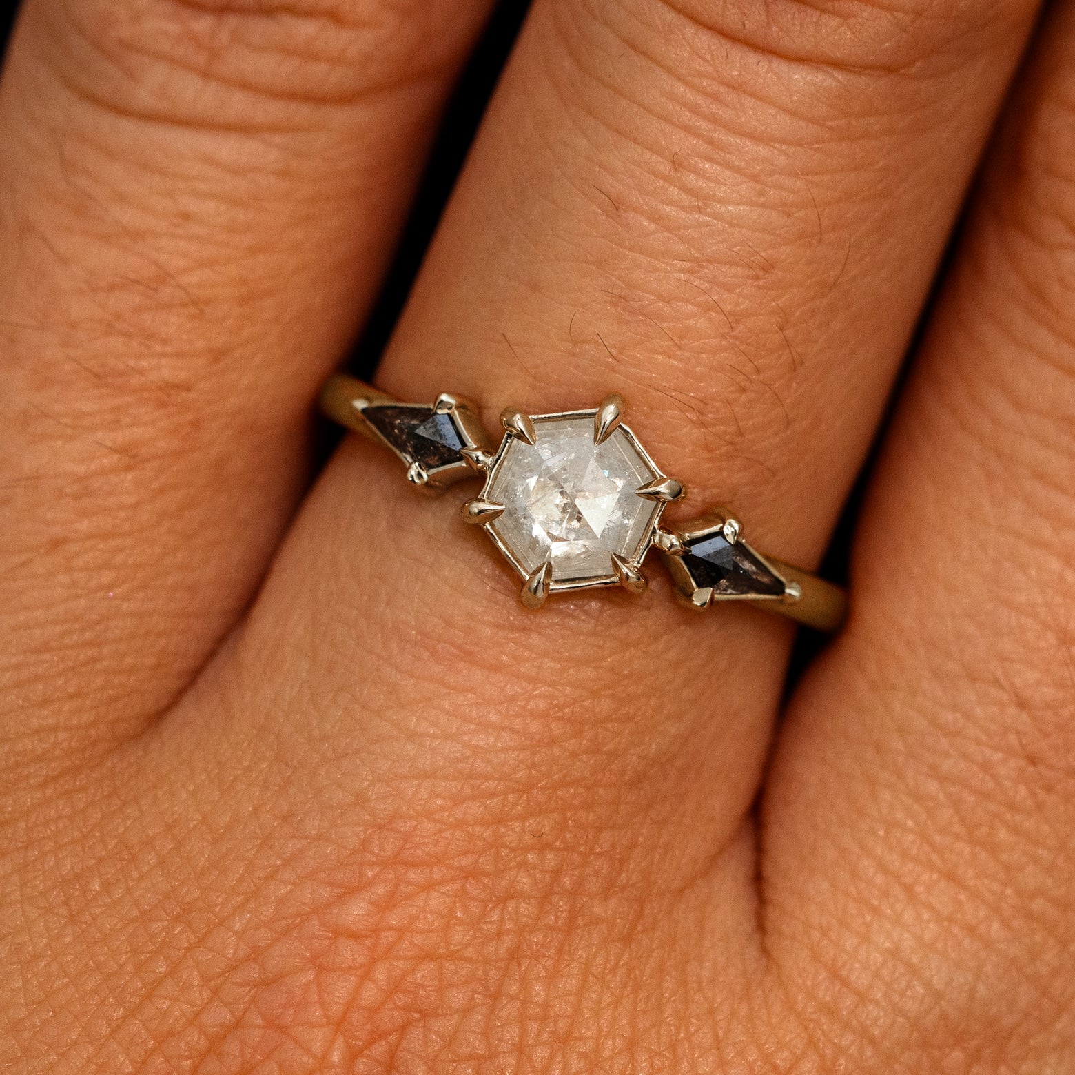 A model's hand wearing a 14k champagne gold Hexagon Salt and Pepper Diamond Black and White Ring