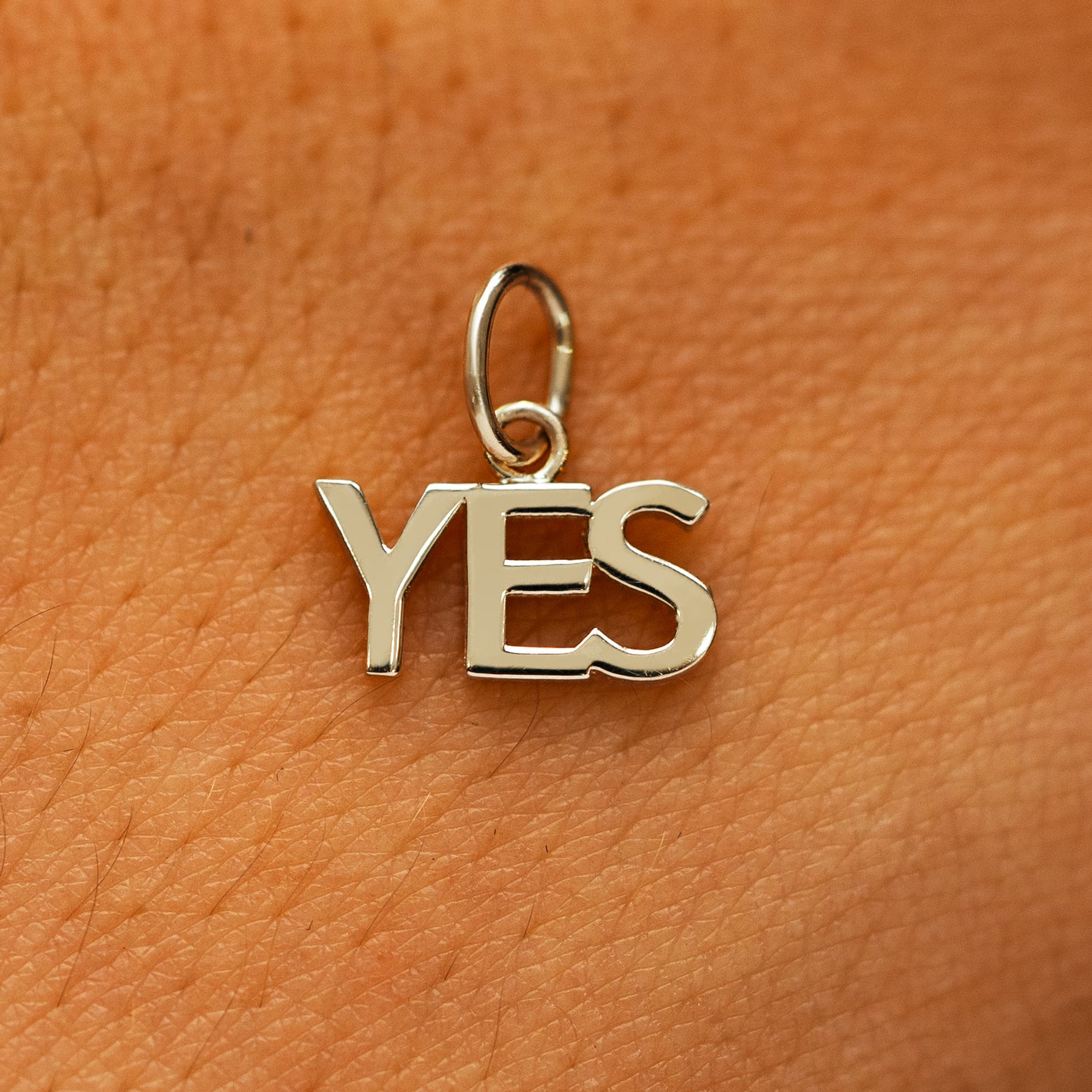 A solid 14k champagne gold Yes Charm on the back of a models hand