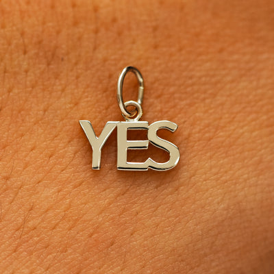 A solid 14k champagne gold Yes Charm on the back of a models hand