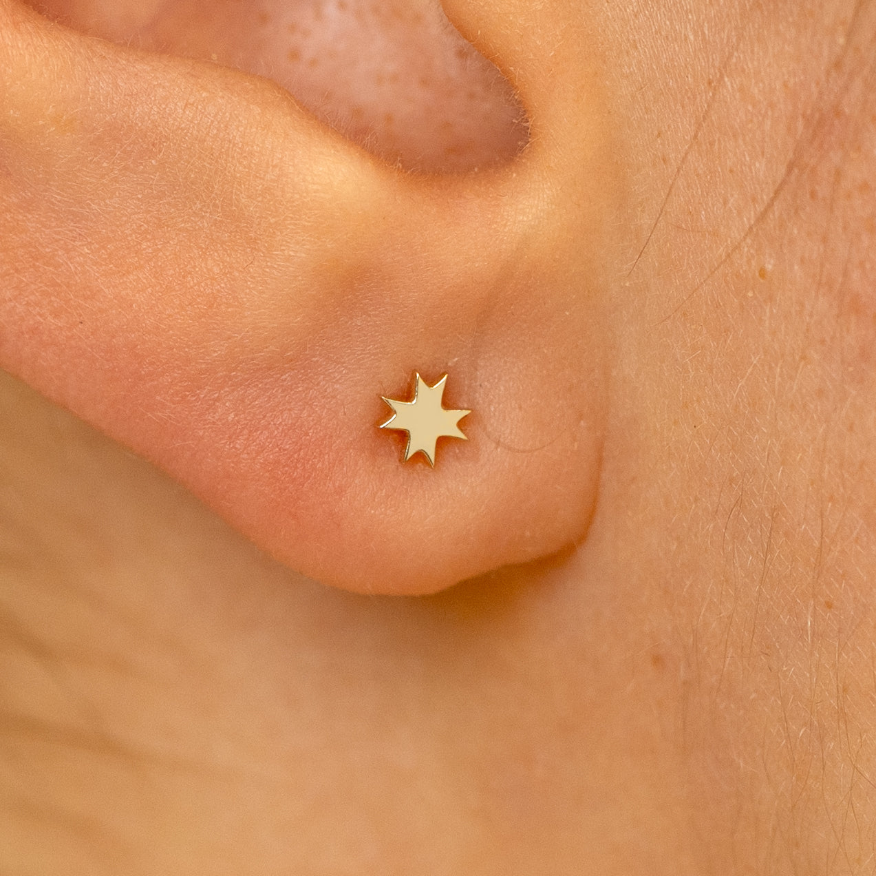 Close up view of a models ear wearing a 14k champagne gold 8 pointed star flatback piercing