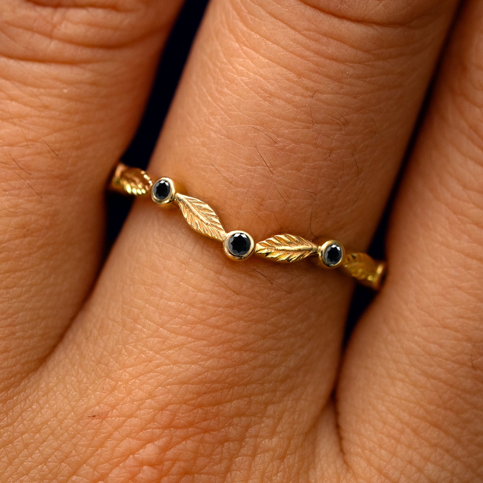 Close up view of a model's fingers wearing a 14k yellow gold Chevron Leaves and Black Diamonds Band