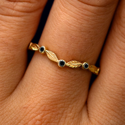 Close up view of a model's fingers wearing a 14k yellow gold Chevron Leaves and Black Diamonds Band