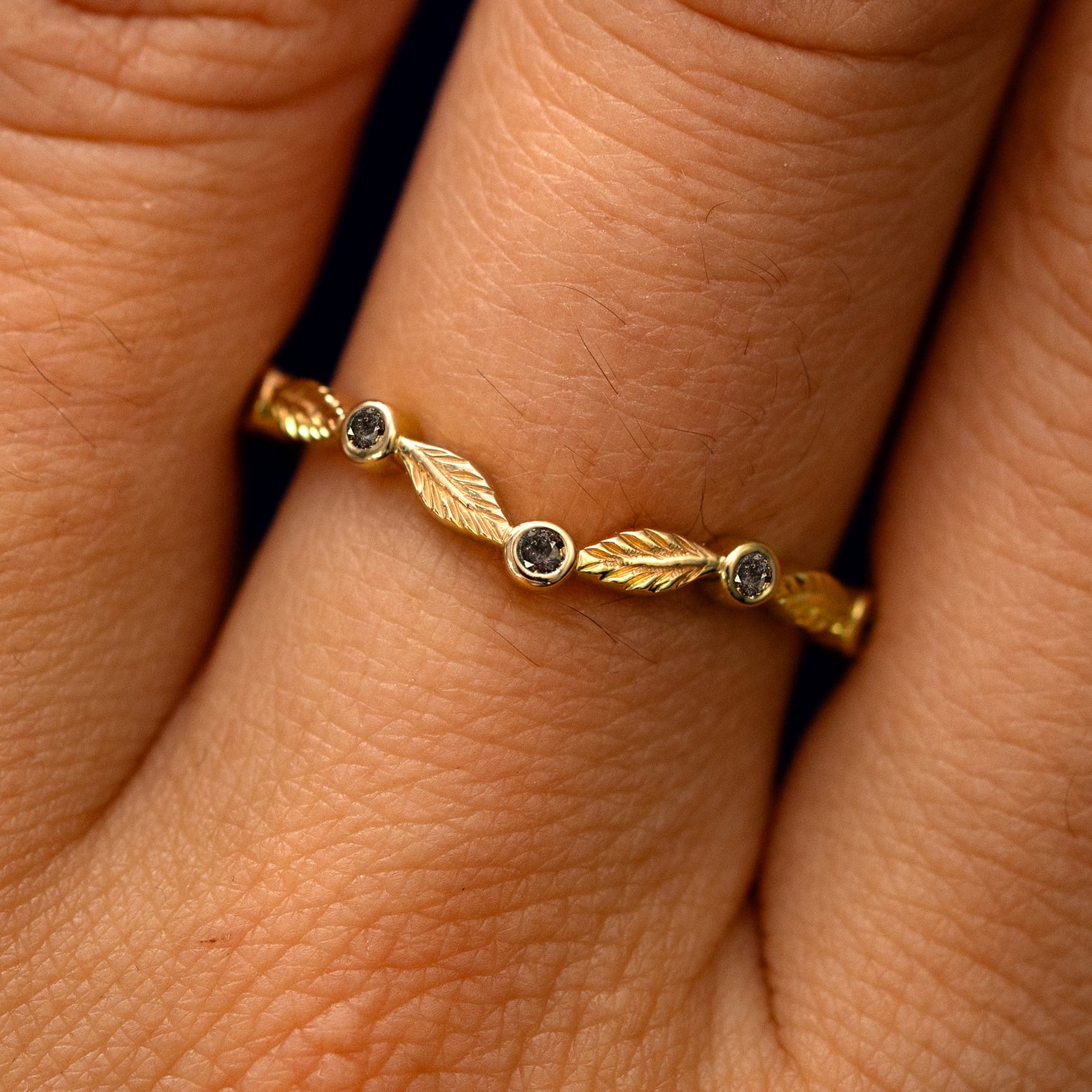 Close up view of a model's fingers wearing a 14k yellow gold Chevron Leaves and Salt and Pepper Diamonds Band